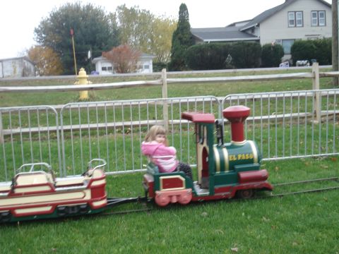 2000 Ford Crown Victoria - A child rides a toy train on a track in a grassy area with a fence and houses in the background.