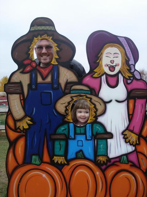 2000 Ford Crown Victoria - A family poses for a photo cutout dressed as scarecrows with pumpkins, likely for a fall or Halloween event.