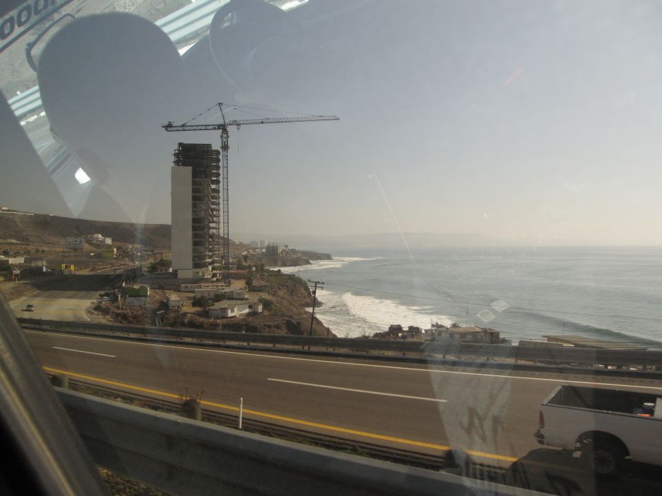 Construction site with a tall building and crane overlooking the ocean and a highway