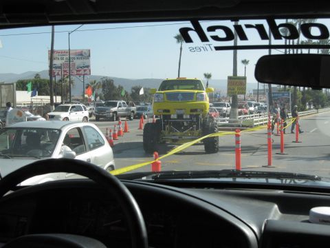 1986 Ford Bronco - A bright yellow monster truck with oversized tires is the focus of this scene, viewed from the perspective of another vehicle.