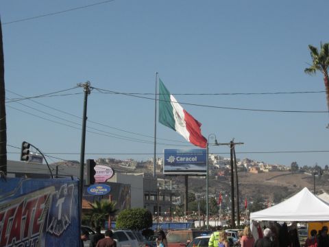 1986 Ford Bronco - A large Mexican flag waves in the breeze above a street scene with buildings and a billboard.