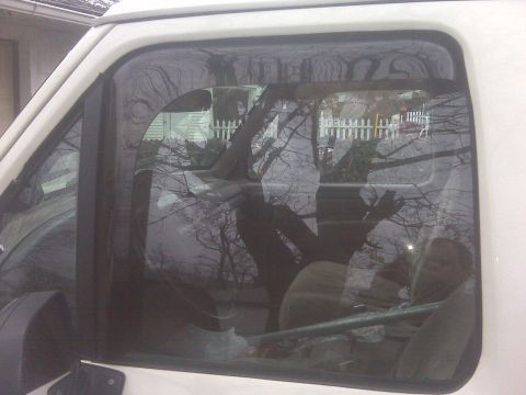 1995 Ford Bronco - The reflection in the window shows trees and a fence, obscuring details of the vehicle's interior.