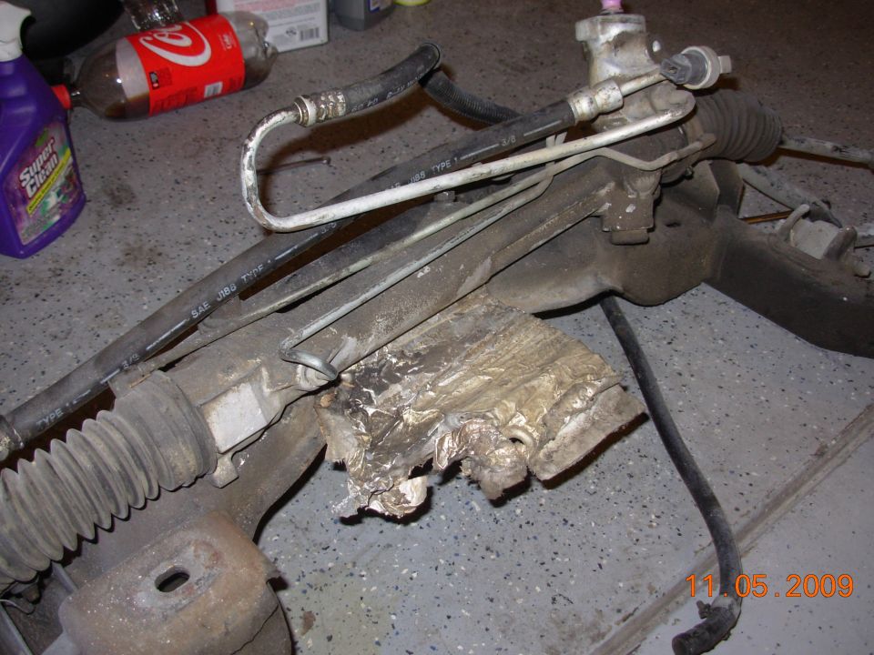 Removed power steering rack assembly with hoses and torn boot on a garage floor