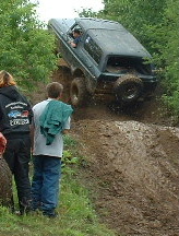 2002 Ford F-350 - An off-road vehicle navigates a challenging muddy incline with spectators watching.