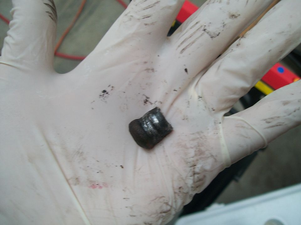 Small worn part held in a dirty white-gloved hand