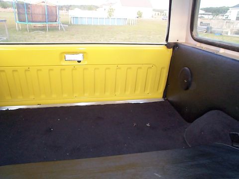 1978 Ford Bronco - The rear interior of a vehicle, showing the cargo area with yellow side panels and black carpet flooring.