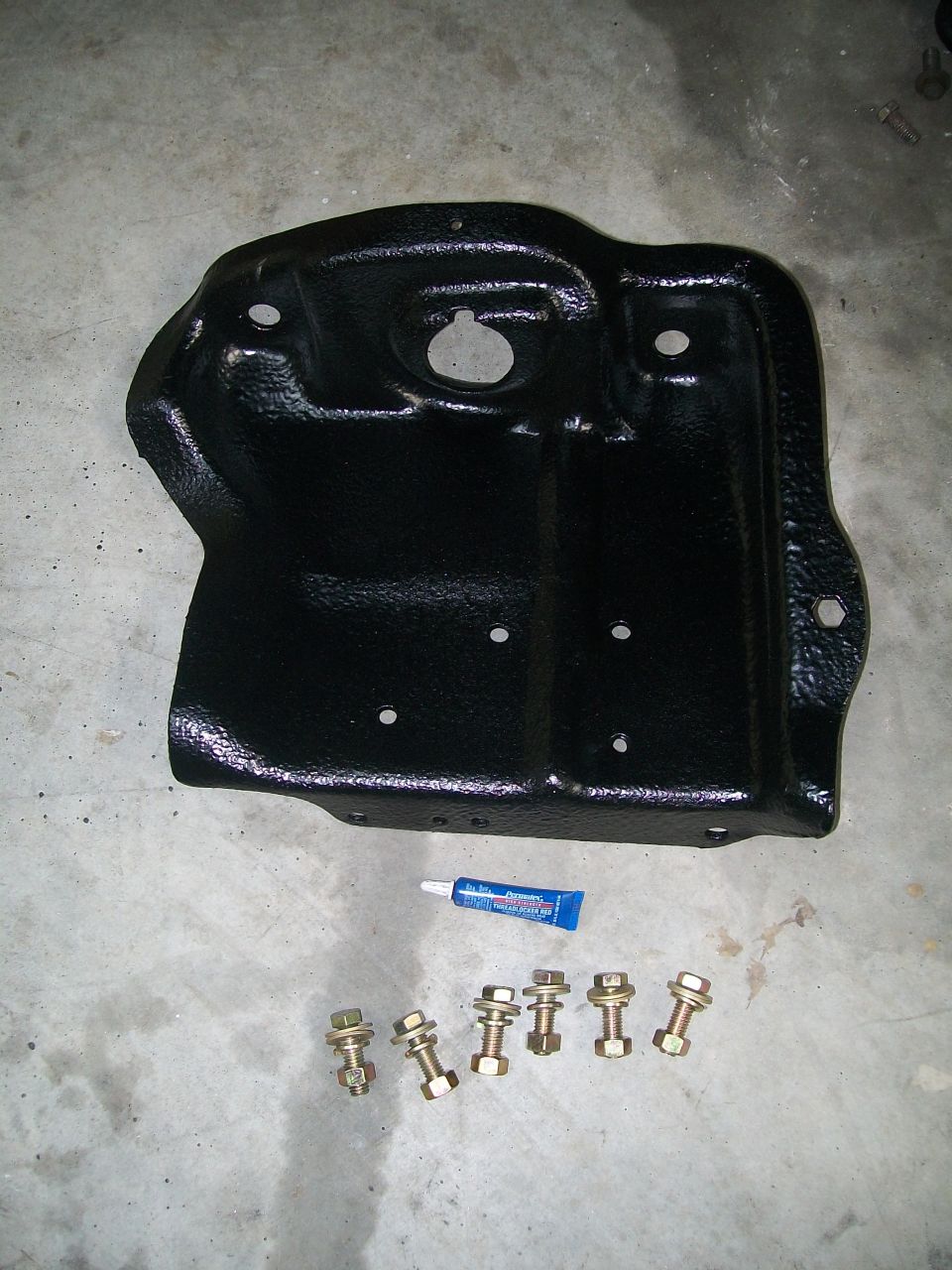 Refinished black engine oil pan with tube of sealant and mounting bolts