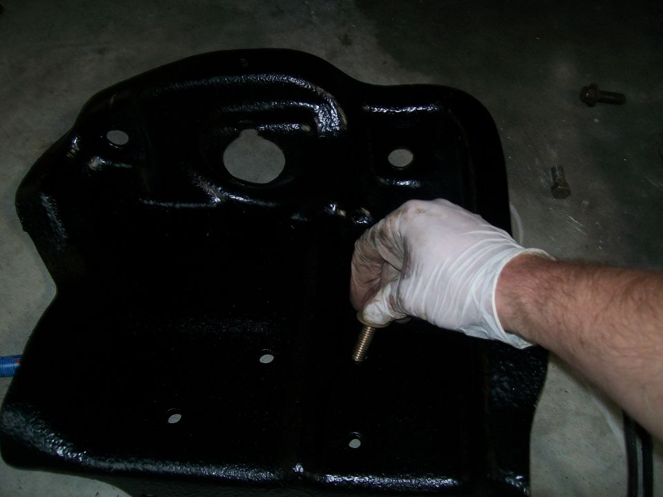 Gloved hand installing a stud into a black oil pan