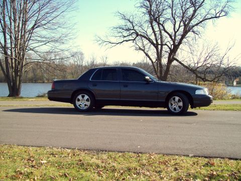 2004 Ford Crown Victoria - A dark sedan, identified as a 2004 Ford Crown Victoria, is parked on the side of a road next to a body of water.