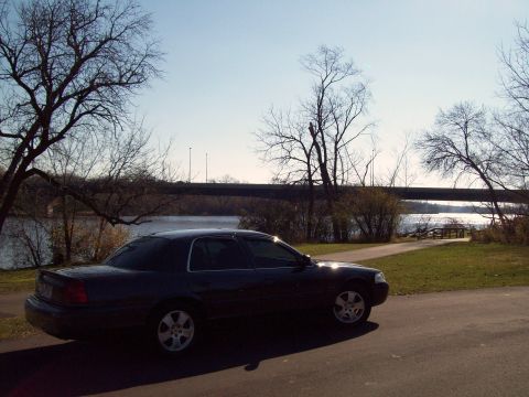 2004 Ford Crown Victoria - A 2004 Ford Crown Victoria sits parked beside a body of water under a clear sky.