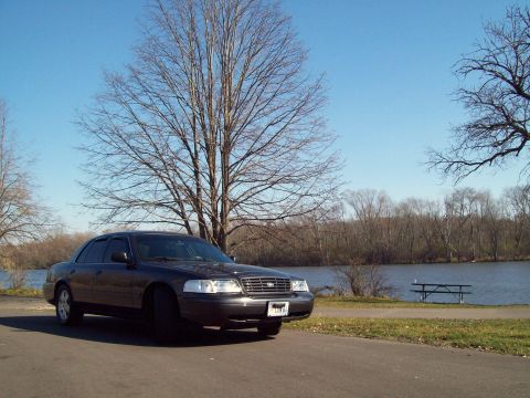 2004 Ford Crown Victoria - A 2004 Ford Crown Victoria sits parked near a body of water on a clear day, with a picnic table visible in the background.