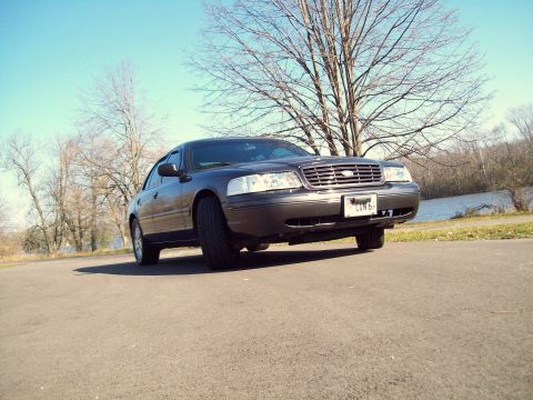 2004 Ford Crown Victoria - A dark sedan is viewed from a low angle, with a body style consistent with a 2003 model year, parked outdoors.