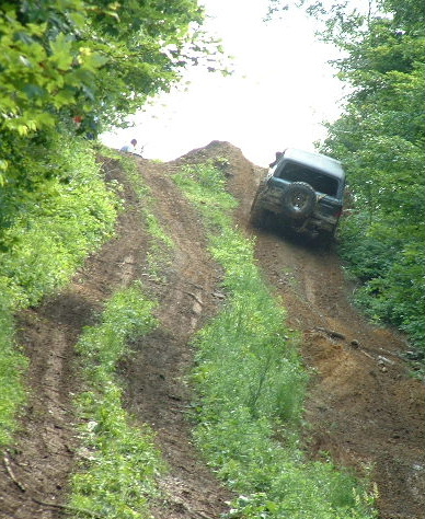 2002 Ford F-350 - Off-road vehicle navigates a challenging dirt incline surrounded by lush green foliage.