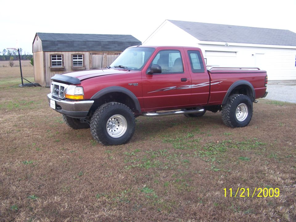Lifted red Ford Ranger extended-cab 4x4 on mud tires parked in a grass yard