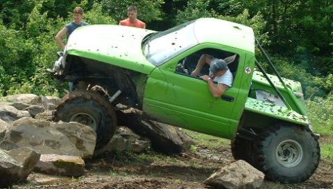 2002 Ford F-350 - A modified truck attempts to climb over large rocks on a muddy trail with onlookers watching.