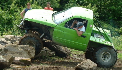 Bright green caged rock buggy built from a pickup cab crawling over large rocks, driver leaning out