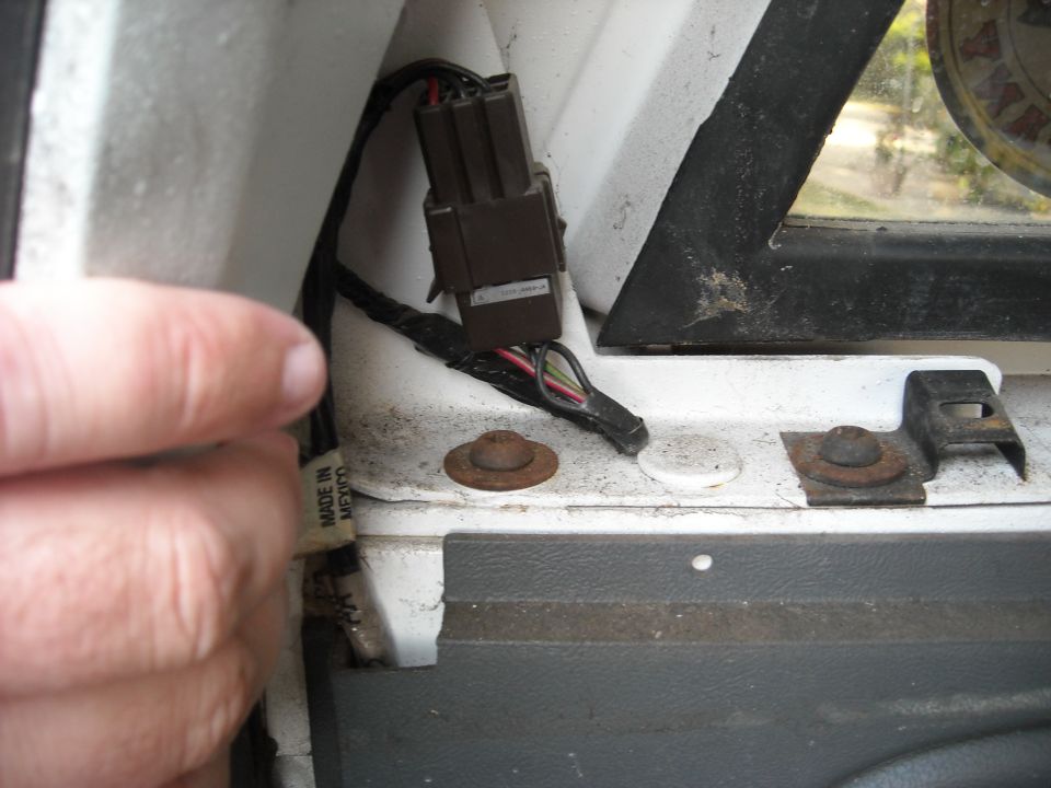 Close-up of a brown electrical connector with wires, near a window frame and rusty fasteners