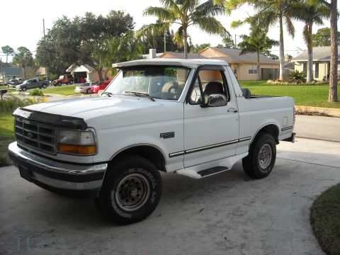 1994 Ford Bronco - This white Ford Bronco, likely a 1992 model, is parked in a suburban driveway with other vehicles visible in the background.