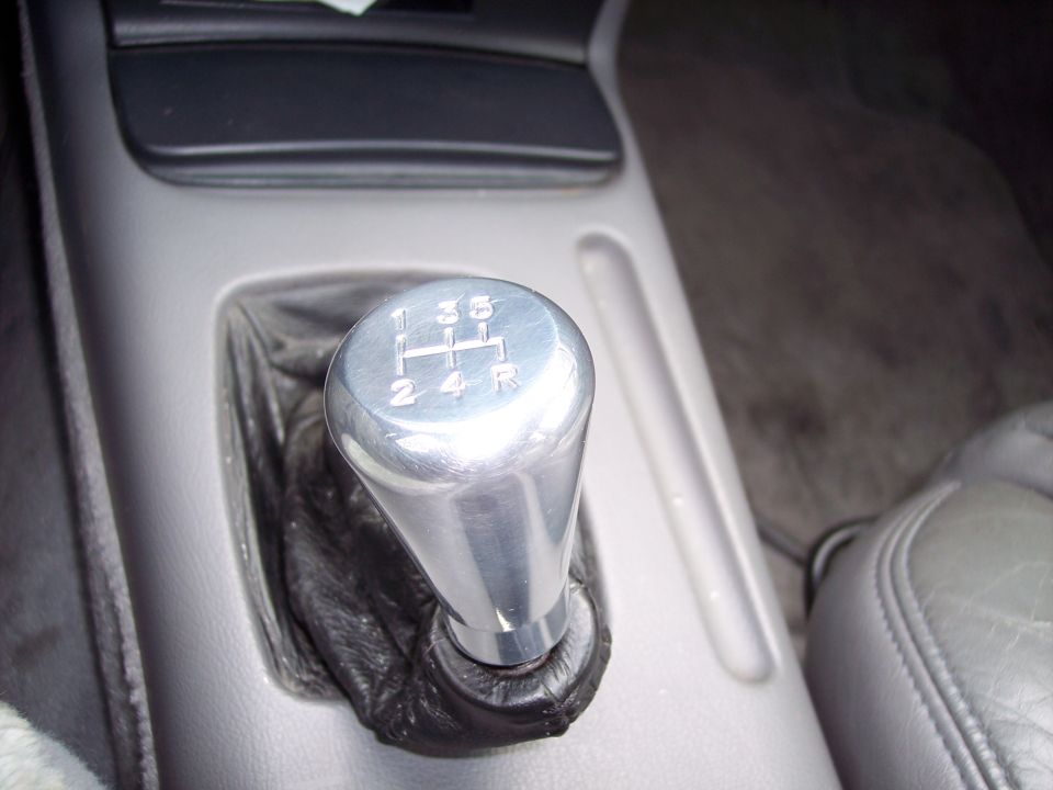 Close-up of a silver manual transmission shift knob with gear pattern (1-3-5, 2-4-R) and black leather boot