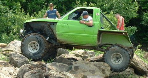 2002 Ford F-350 - A heavily modified truck is being driven over a challenging rocky terrain with people observing.