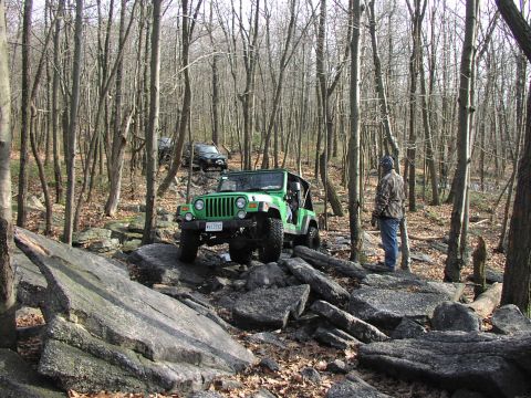 1986 Ford Bronco - Off-roading in a forest with multiple vehicles navigating a challenging rocky path.