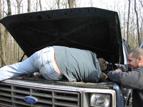 1986 Ford Bronco - A person works on the engine of a 1986 Ford Bronco while another person watches.