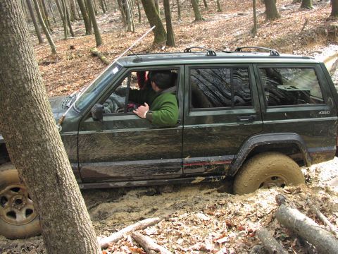 1986 Ford Bronco - A Jeep Cherokee XJ is stuck deep in mud while off-roading in a wooded area.
