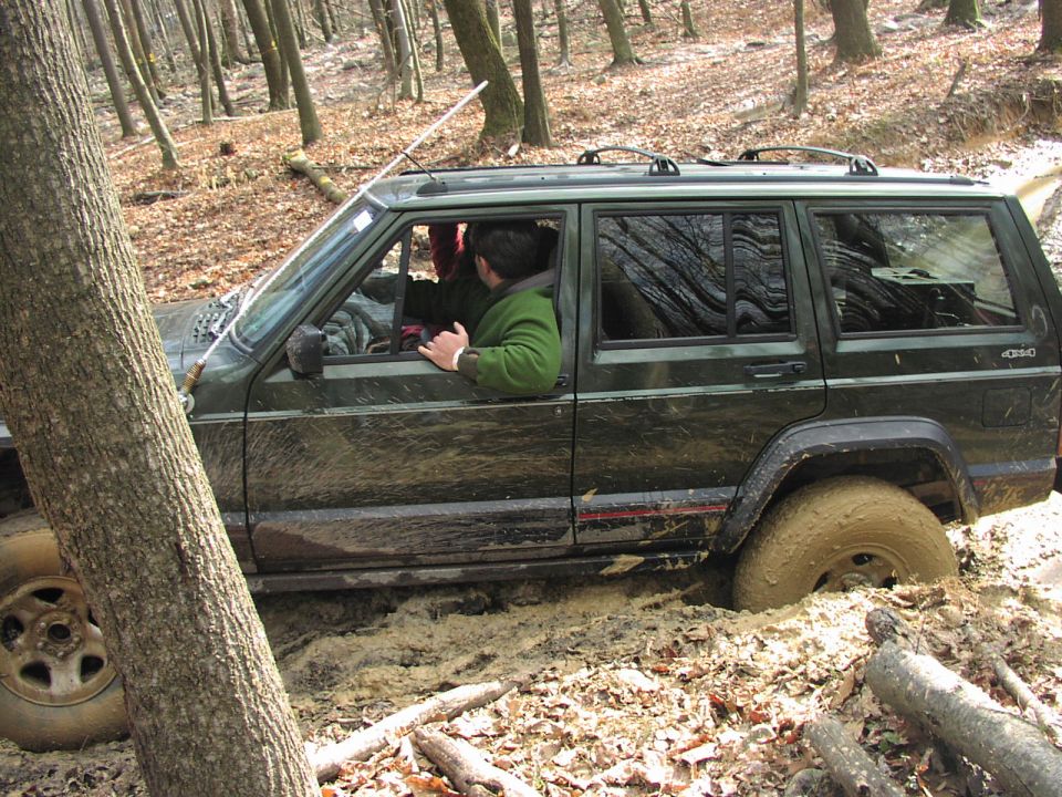 Green Jeep Cherokee XJ stuck in mud off-road, driver visible