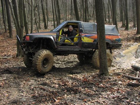 1986 Ford Bronco - Customized off-road vehicle navigates a muddy trail in a wooded area.