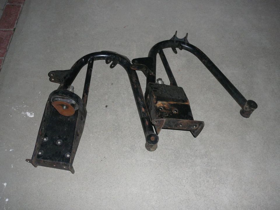 Black metal vehicle suspension components with rusty orange reflectors on a concrete surface