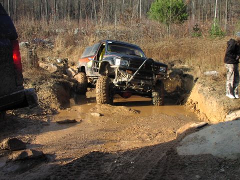 1986 Ford Bronco - This modified SUV is tackling a challenging mud obstacle on an off-road trail.
