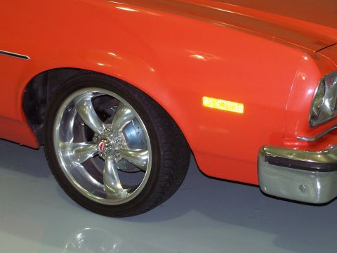 1973 Ford Ranchero - Front quarter detail of a lowered orange car indoors on a light gray floor, showing a polished five-spoke billet wheel with a red center ca…