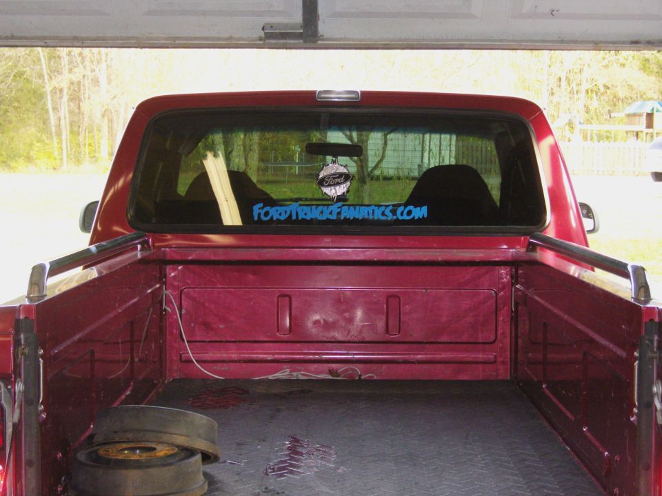 Red pickup truck bed and rear window with "FORDTRUCKFANATICS.COM" sticker