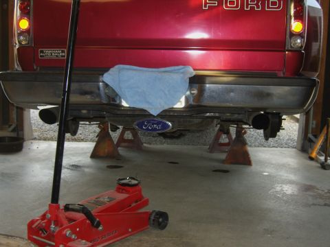 2007 Ford Mustang - The rear of a red Ford pickup truck is shown elevated on jack stands, with a hydraulic jack in the foreground.