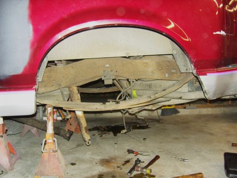 2007 Ford Mustang - The rear suspension of a red pickup truck is shown while on jack stands, with leaf springs and frame components visible.