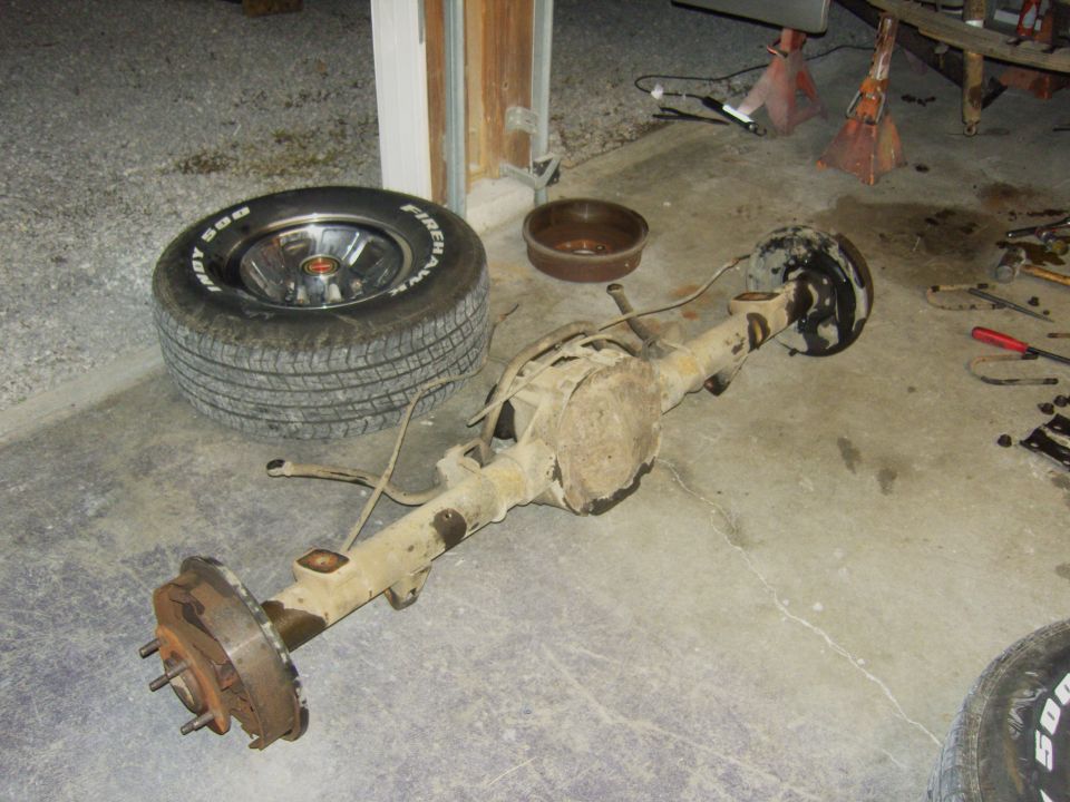 Rear axle assembly, a Firestone tire on a chrome rim, and a brake drum on a concrete floor