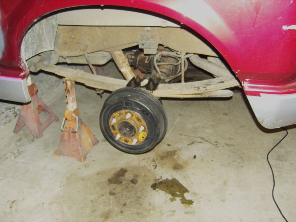 Rear axle and leaf springs on a vehicle supported by jack stands. One wheel is removed