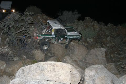 1996 Ford Bronco - Off-road race truck with number 302 navigating difficult rocky terrain at night.