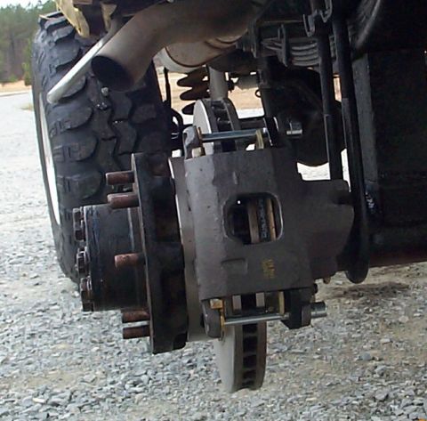 1978 Ford Bronco - The rear brake system of a vehicle, showing the caliper, rotor, and part of the tire.
