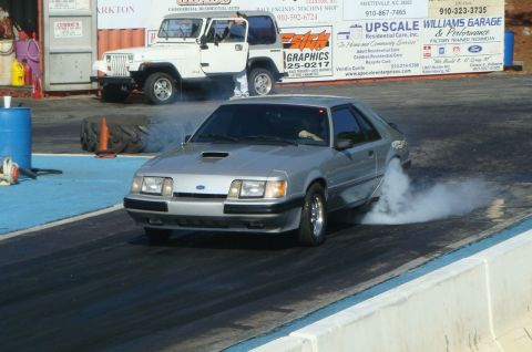 1986 Ford Mustang - Silver 1986 Ford Mustang performing a burnout on the drag strip, with a Jeep visible behind it.