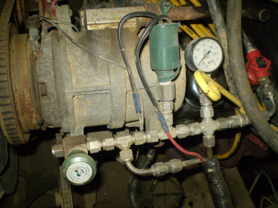 Close-up of engine part with two pressure gauges and green solenoid