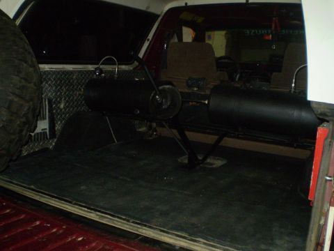 1986 Ford Bronco - The cargo area of an SUV shows a spare tire and two large black tanks mounted on the floor.
