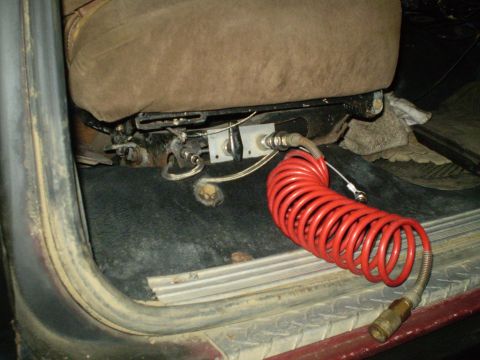 1986 Ford Bronco - An air hose is connected to the seat mounting hardware inside a vehicle.