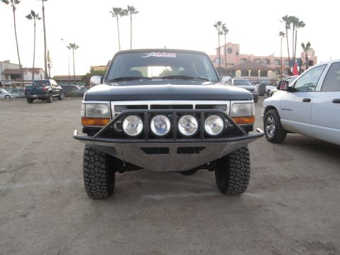 1986 Ford Bronco - A modified Ford Bronco from the early to mid-1990s is parked outdoors, with other vehicles and buildings in the background.