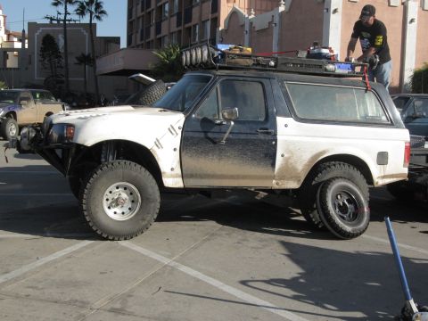 1986 Ford Bronco - Modified 1986 Ford Bronco with off-road tires and a roof rack, seen in a parking lot.