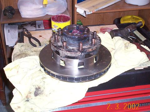 1978 Ford Bronco - A close-up of a vehicle's wheel hub and brake rotor, with tools and grease nearby.