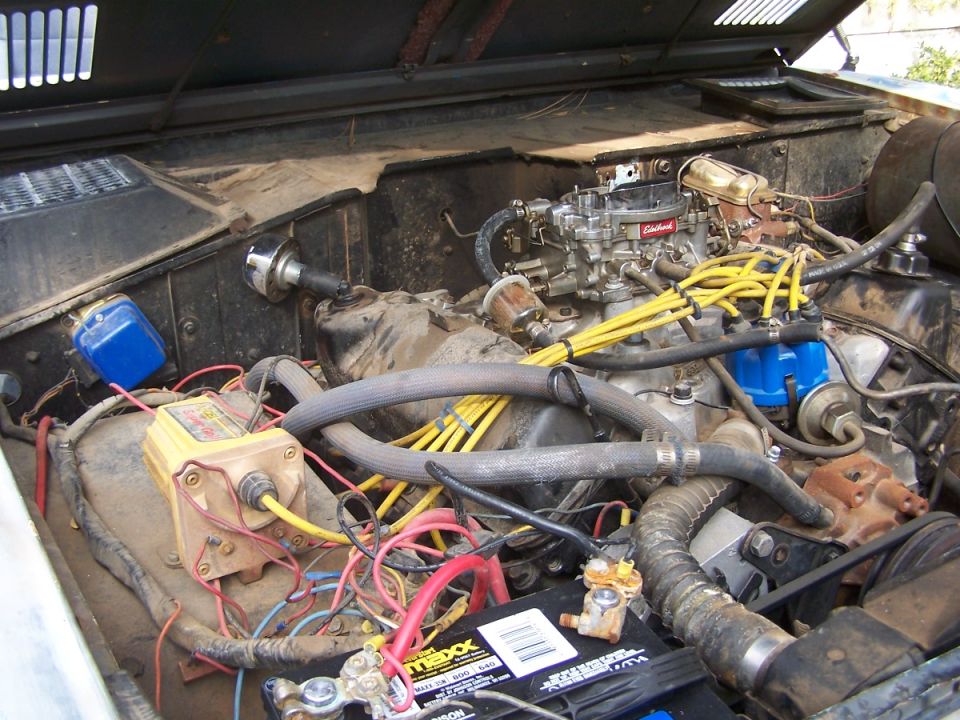 Engine bay showing carburetor, yellow spark plug wires, blue distributor cap, and battery