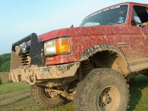 2002 Ford F-350 - This heavily muddied red Ford truck is shown from the front 3/4 angle, with a bull bar and off-road tires.