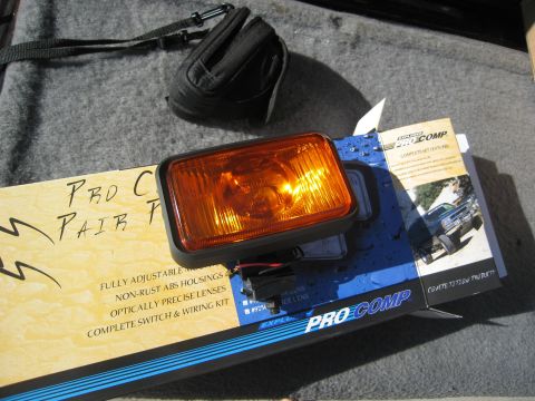 1986 Ford Bronco - A rectangular Pro Comp Explorer off-road driving light with an amber lens and black ABS housing, resting on its blue-and-white retail box w…