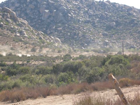 1986 Ford Bronco - A vehicle races across a dusty desert landscape, kicking up a plume of dust.